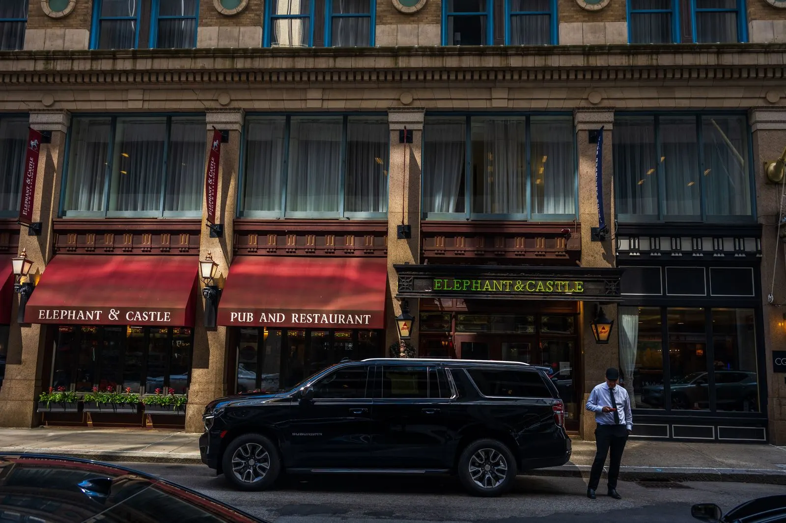 An executive SUV waiting outside a restaurant in the evening with the chauffeur beside it